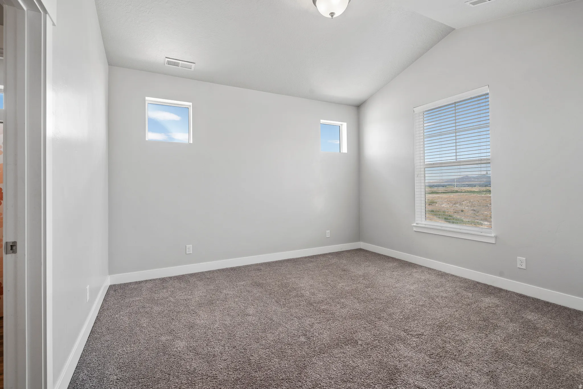Carpeted empty room with lofted ceiling and baseboards