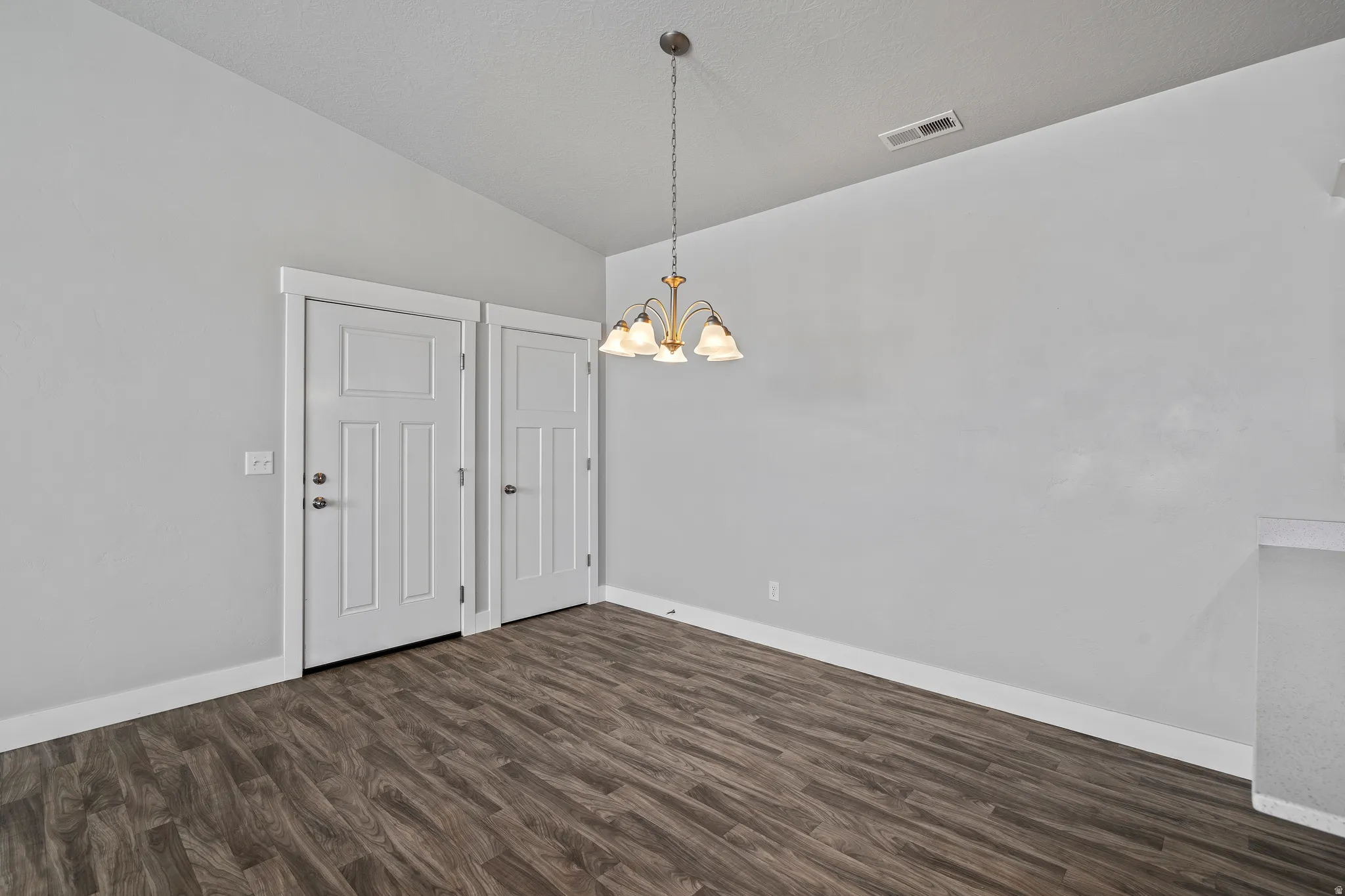 Unfurnished dining area featuring lofted ceiling, dark wood-style flooring, and hanging lights