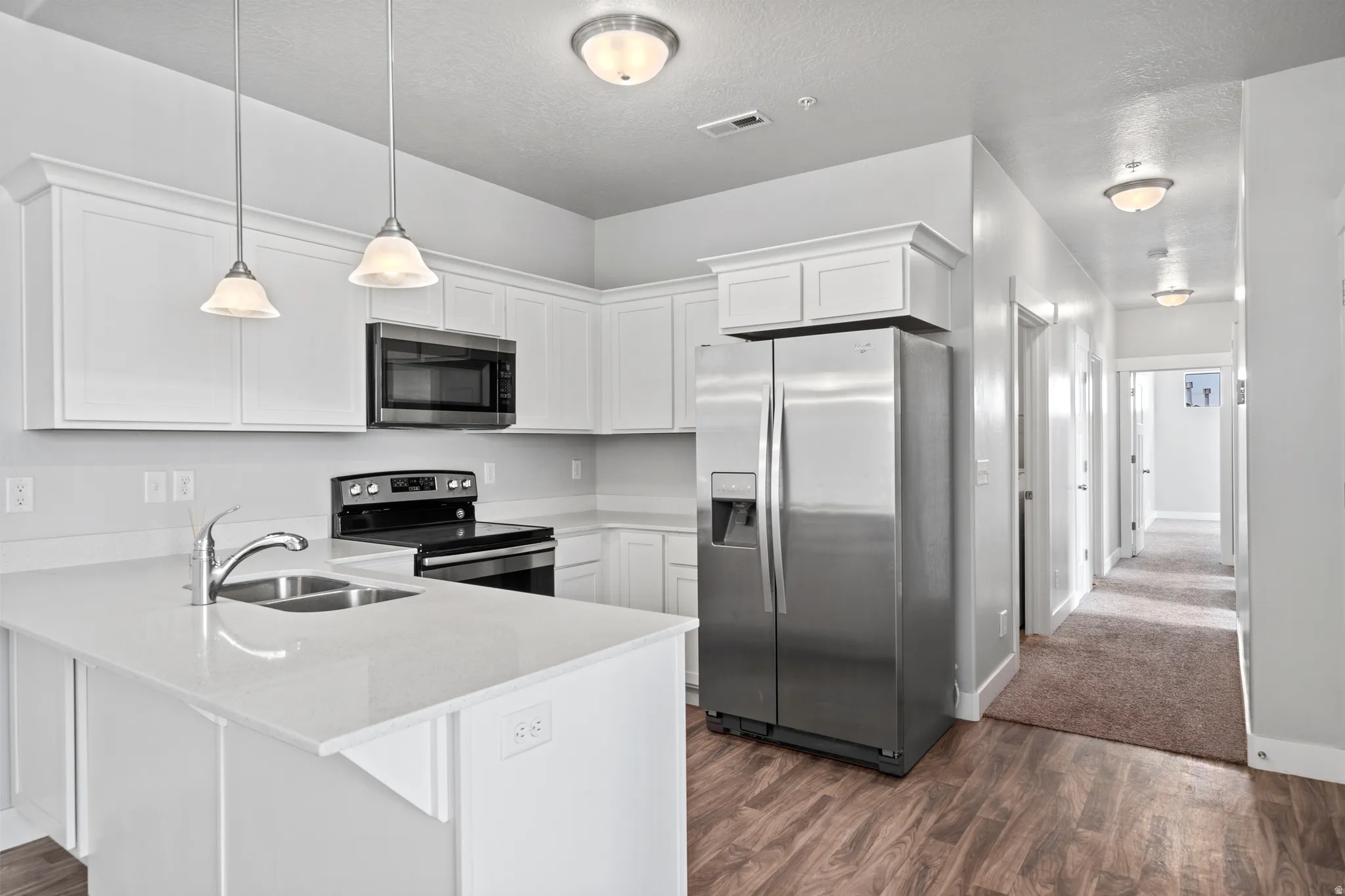 Kitchen featuring stainless steel appliances, white cabinetry, dark wood-type flooring, a peninsula, and a textured ceiling