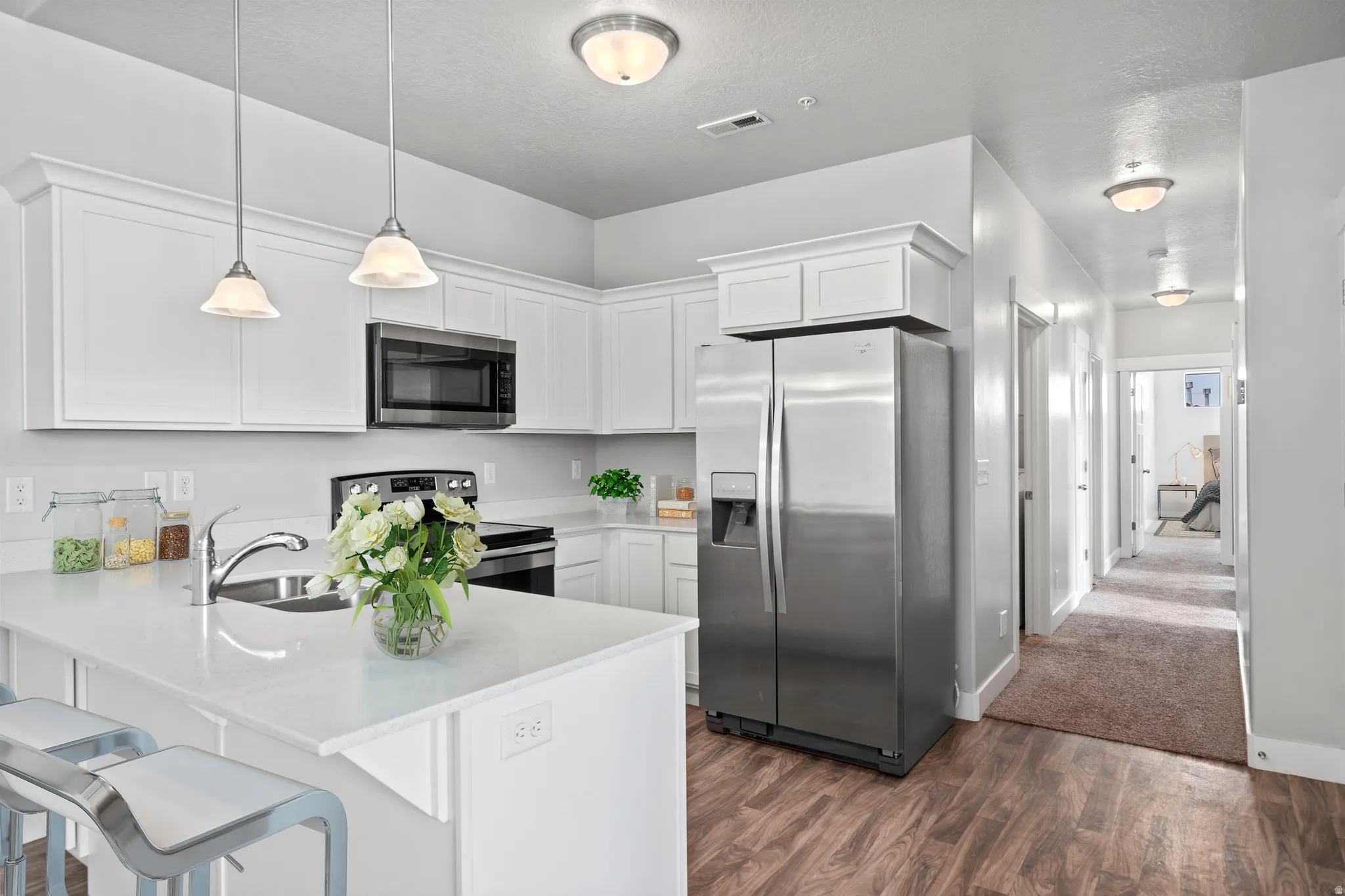 Kitchen featuring stainless steel appliances, a kitchen bar, white cabinets, a peninsula, and a textured ceiling
