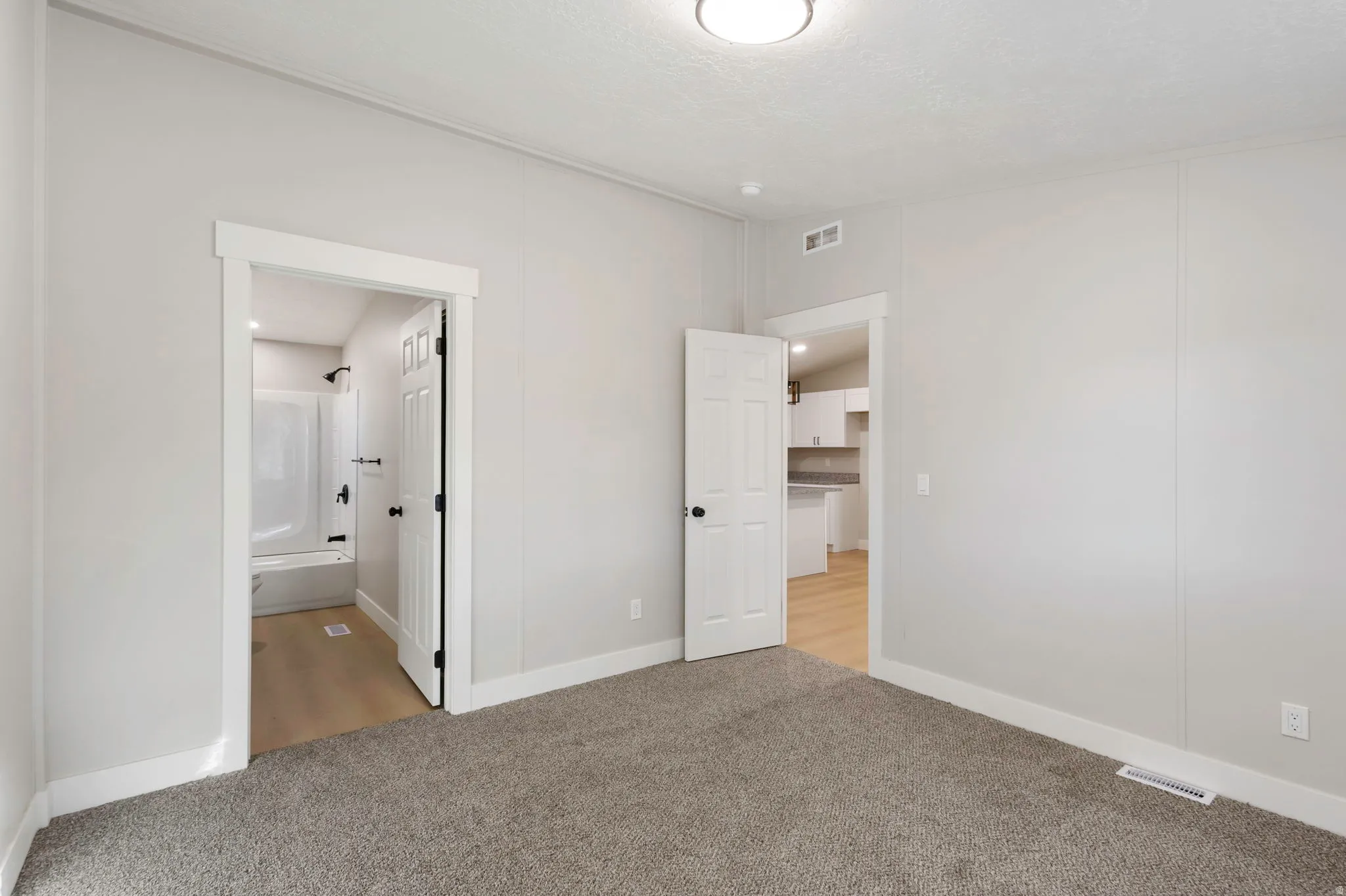Unfurnished bedroom featuring light colored carpet, ensuite bath, and lofted ceiling
