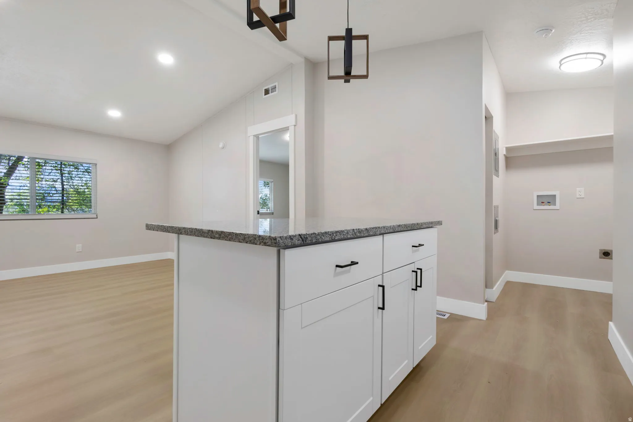 Kitchen with lofted ceiling, pendant lighting, light wood-style flooring, white cabinetry, and a kitchen island
