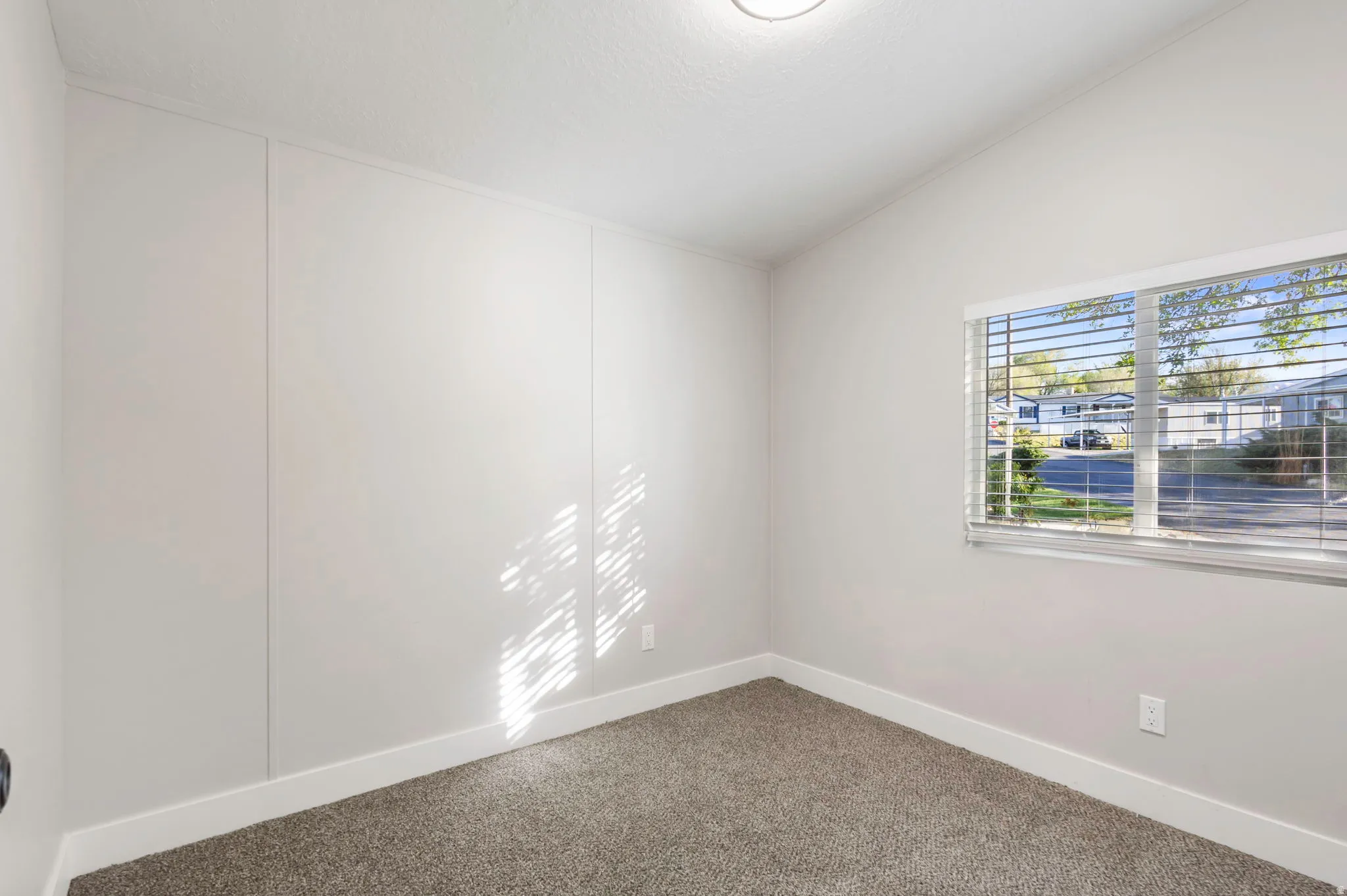 Carpeted empty room featuring vaulted ceiling and baseboards