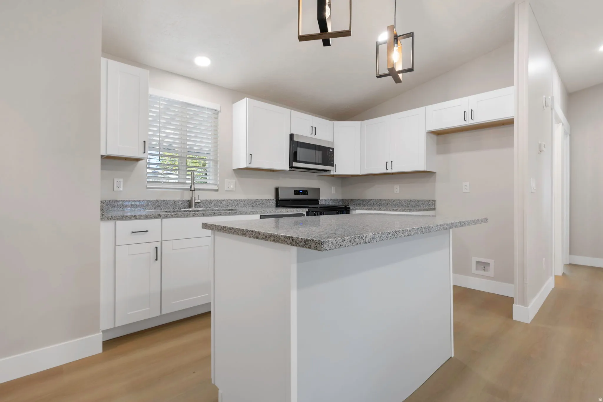 Kitchen with white cabinets, stainless steel appliances, hanging light fixtures, a center island, and light wood finished floors