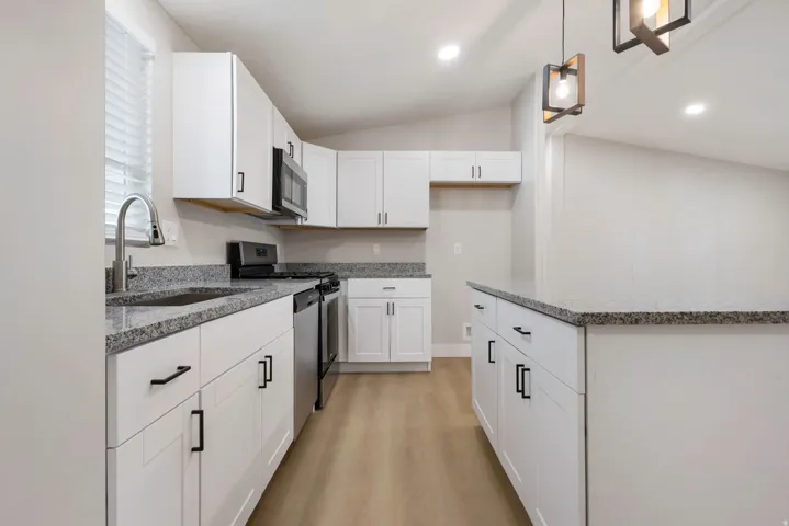 Kitchen with white cabinetry, light wood-type flooring, light stone countertops, a kitchen island, and stainless steel appliances