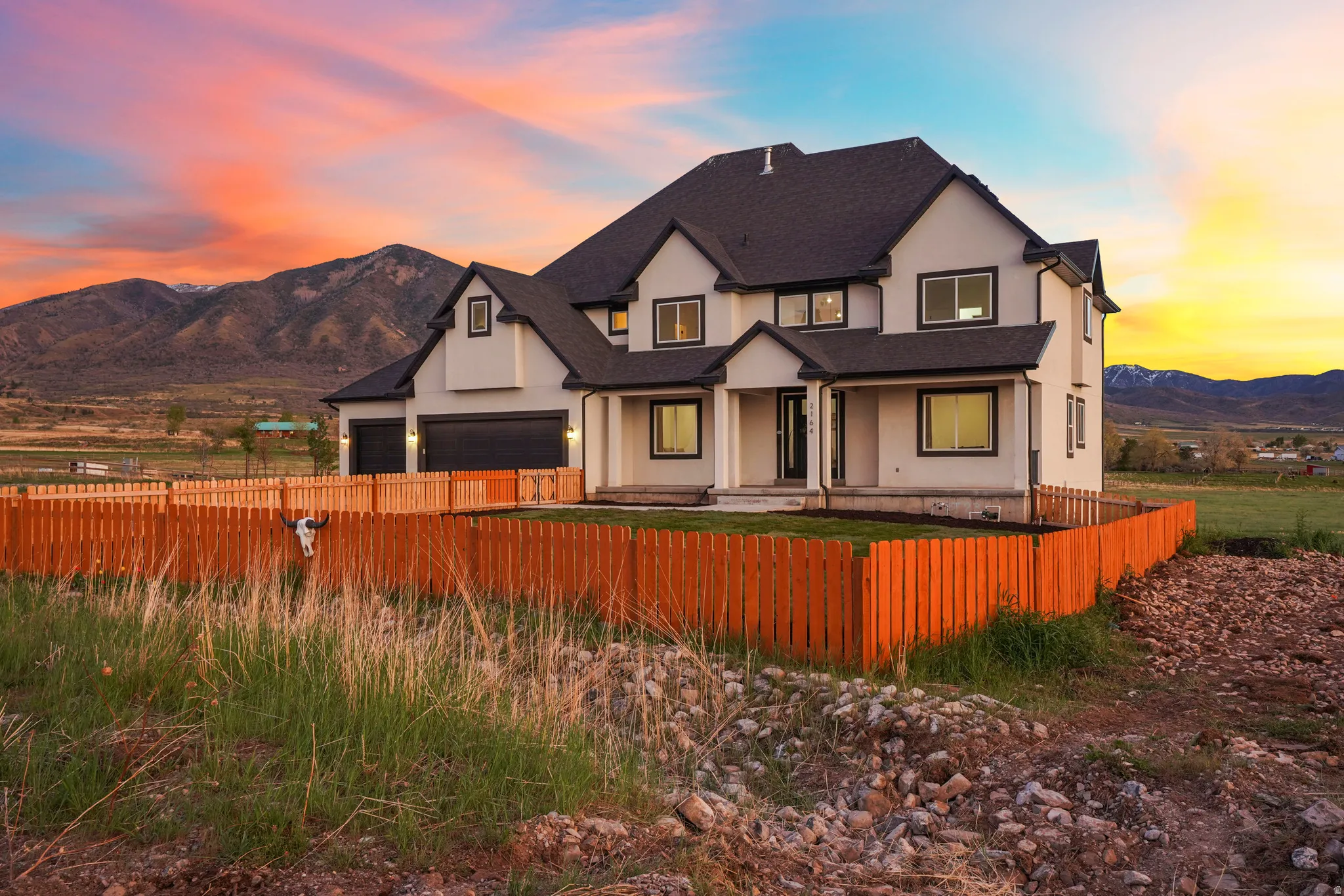 Modern inspired farmhouse featuring a fenced front yard, a mountain view, a garage, covered porch, and stucco siding