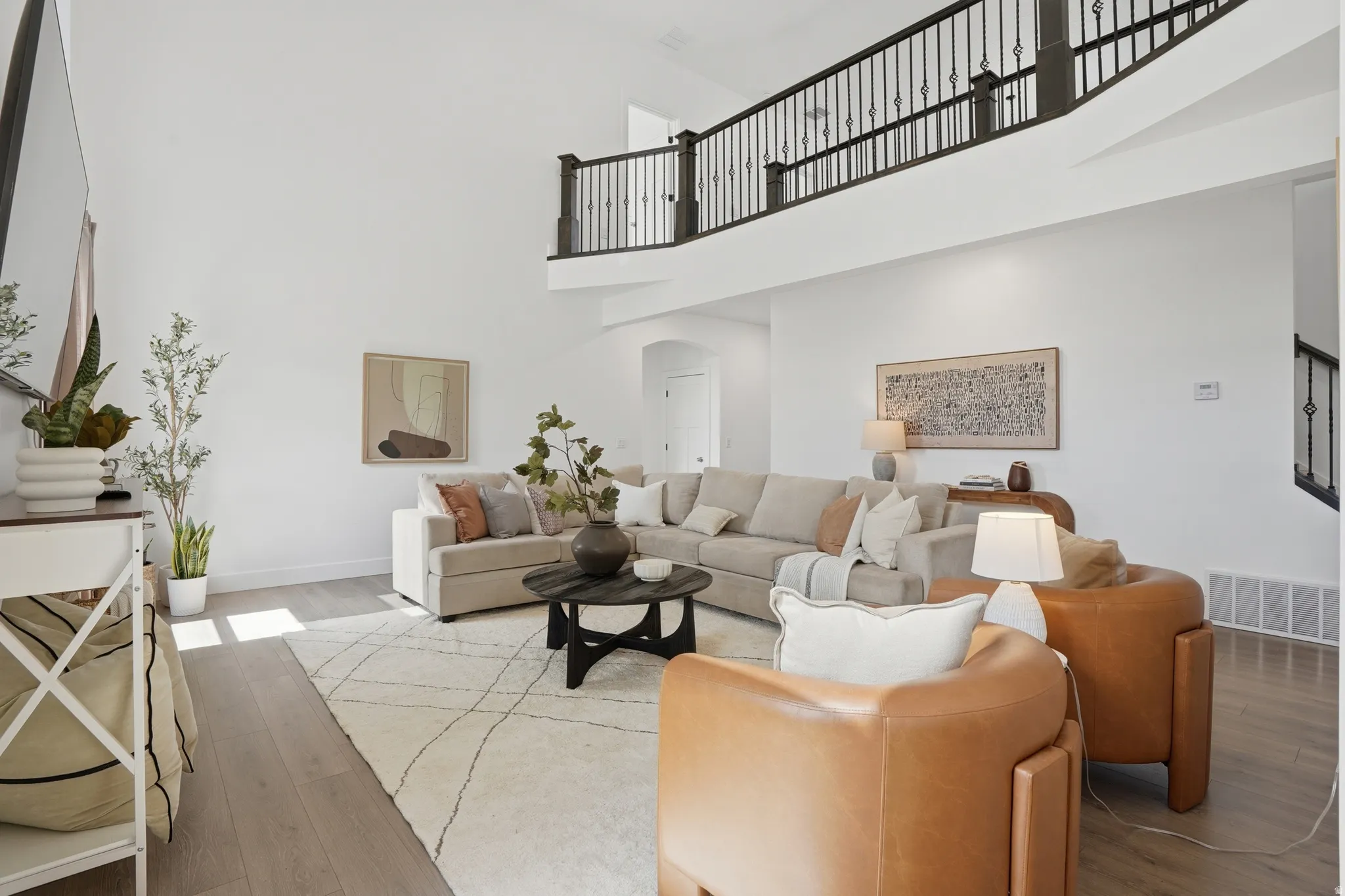 Living room with arched walkways, light wood-style floors, and a high ceiling