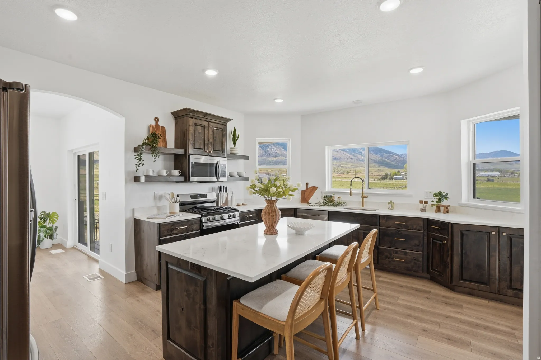 Kitchen with dark wood finish cabinets, arched walkways, a kitchen island, open shelves, and light wood finished floors