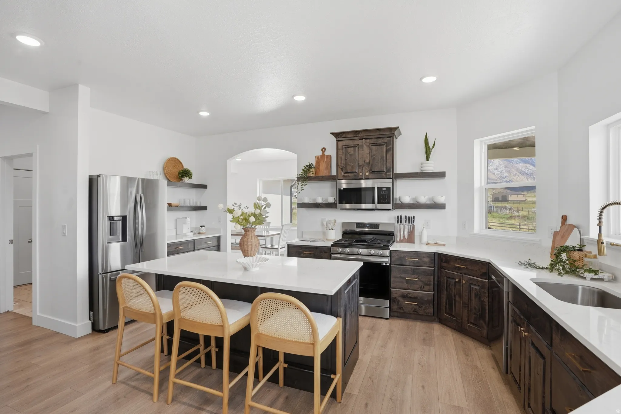 Kitchen featuring open shelves, stainless steel appliances, a kitchen island, arched walkways, and dark wood finish cabinetry