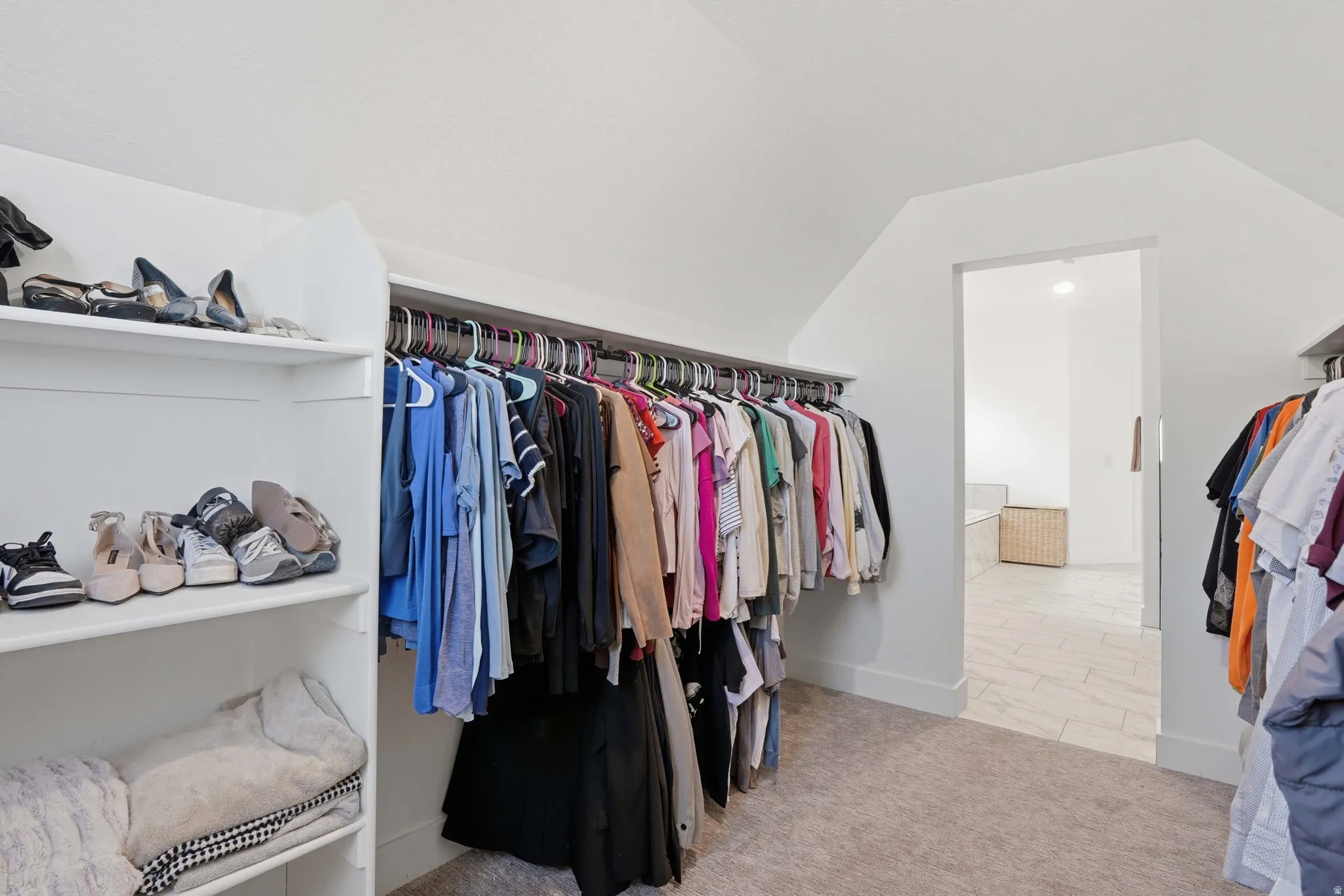 Walk in closet with vaulted ceiling and light colored carpet