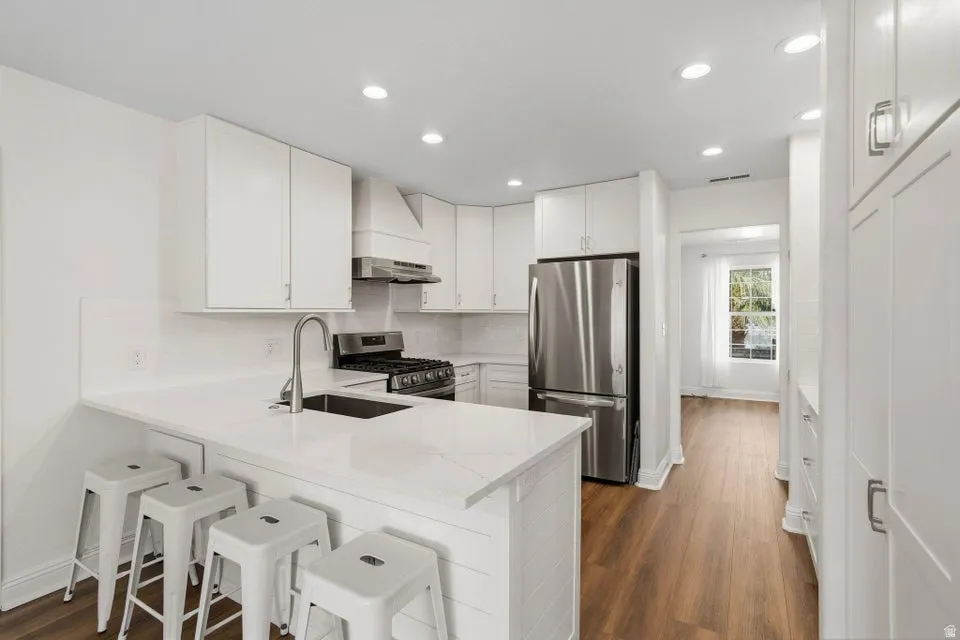 Kitchen featuring a breakfast bar, stainless steel appliances, white cabinetry, recessed lighting, and a peninsula