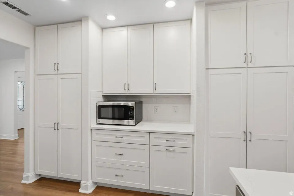 Kitchen featuring white cabinetry, backsplash, stainless steel microwave, and recessed lighting