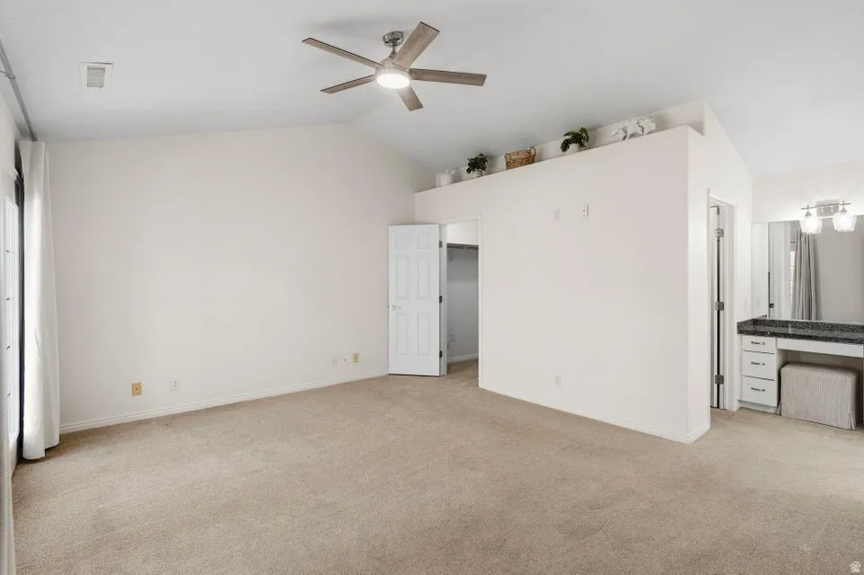 Unfurnished bedroom featuring lofted ceiling, light colored carpet, and a ceiling fan
