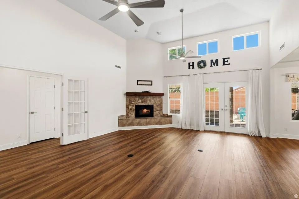 Unfurnished living room featuring french doors, a high ceiling, dark wood-type flooring, a ceiling fan, and a stone fireplace