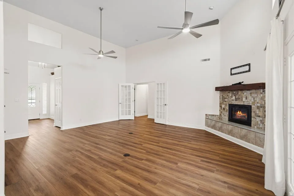Unfurnished living room with a high ceiling, a fireplace, french doors, dark wood-style flooring, and a ceiling fan