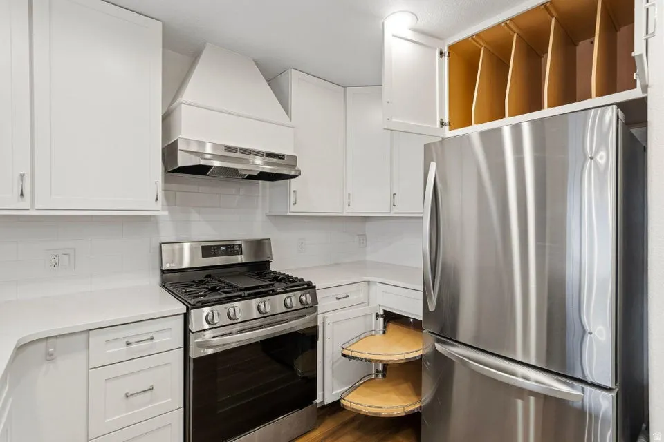 Kitchen featuring stainless steel appliances, white cabinetry, decorative backsplash, and dark wood-style floors