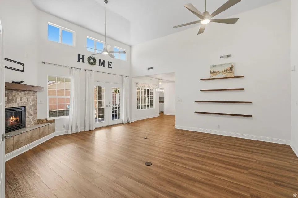 Unfurnished living room featuring french doors, a glass covered fireplace, a high ceiling, dark wood-style floors, and a ceiling fan