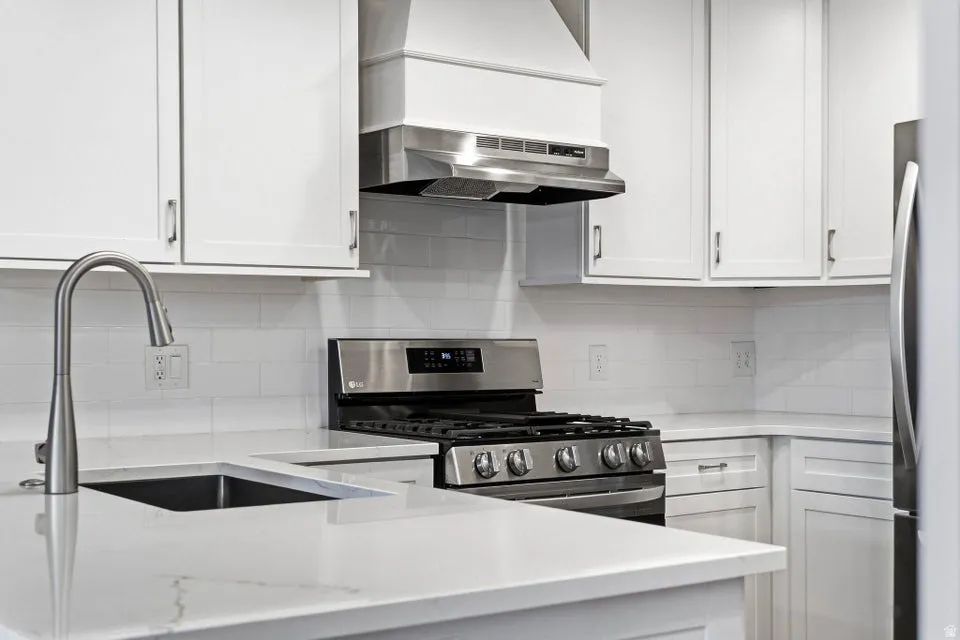 Kitchen featuring stainless steel appliances, white cabinets, light stone countertops, and ventilation hood
