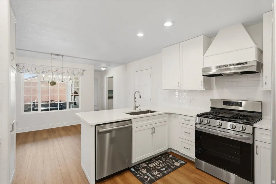 Kitchen with stainless steel appliances, a peninsula, backsplash, white cabinetry, and light wood-type flooring
