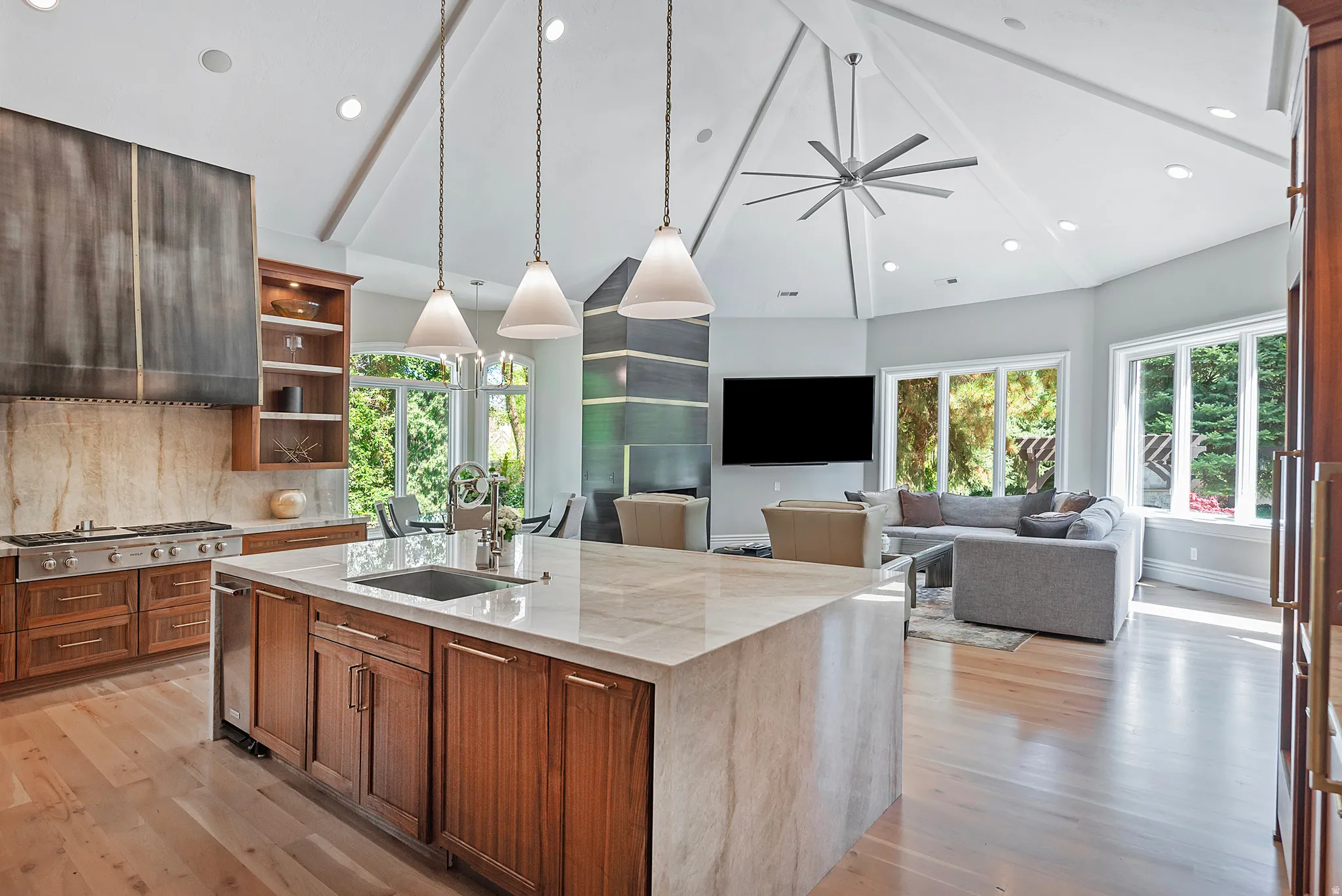 A true bespoke Kitchen with light stone countertops, a center island with sink, wood finish cabinetry, light wood-style floors, brushed metal gas fireplace and lovely family gathering room, plus dining cove.