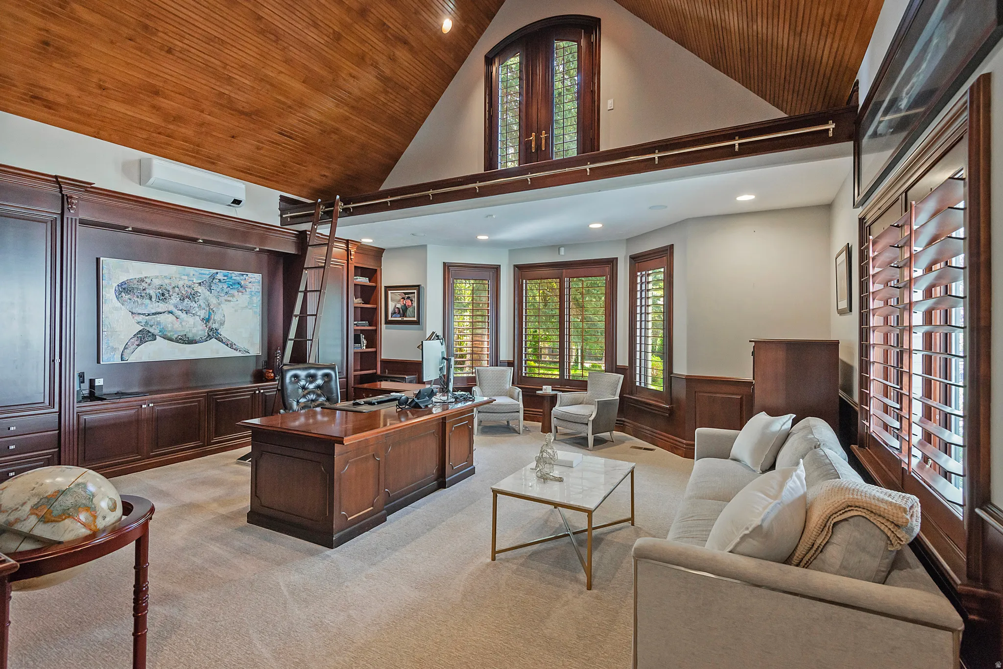 Library/Office with a vaulted wooden panel ceiling, wainscoting, custom wood built ins, and a charming loft with ladder, plantation shutters.