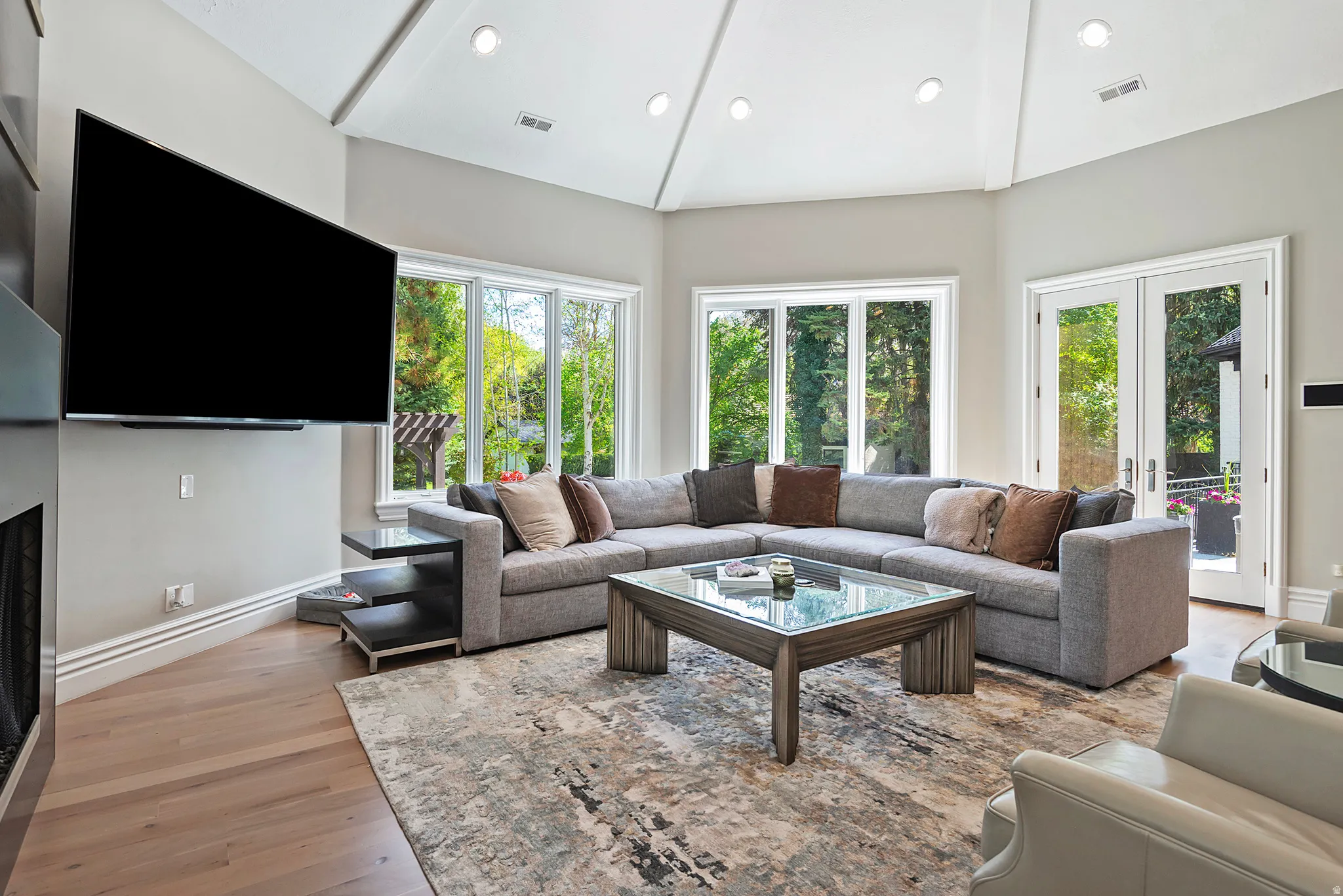 Living room featuring french doors, light wood finished floors, a custom gas fireplace, and opens to the expansive patios and pool.