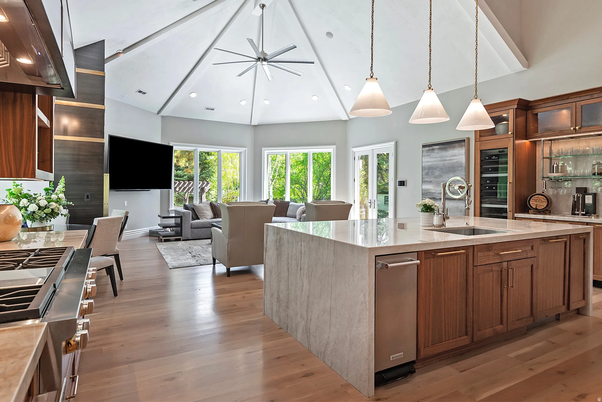 Kitchen with glass insert cabinets, light stone countertops, range hood, wood finish cabinets, and open floor plan
