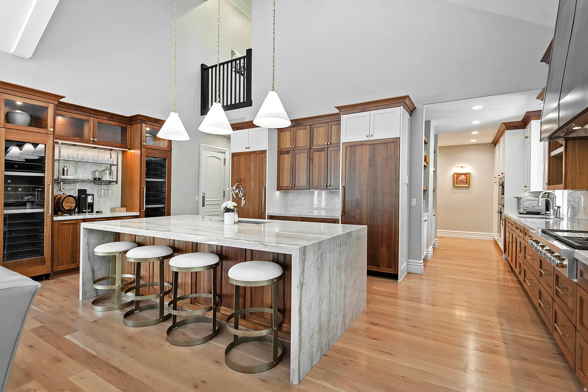 Two tone kitchen with light stone counters, decorative backsplash, a spacious island, a kitchen breakfast bar, built in coffee bar and light wood-style flooring