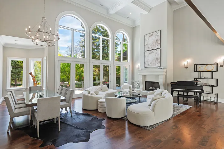Living room featuring ornamental molding, a  cast stone fireplace with raised hearth, dark wood-style flooring, coffered ceiling, large dining area, and soaring 2-story Palladium windows!