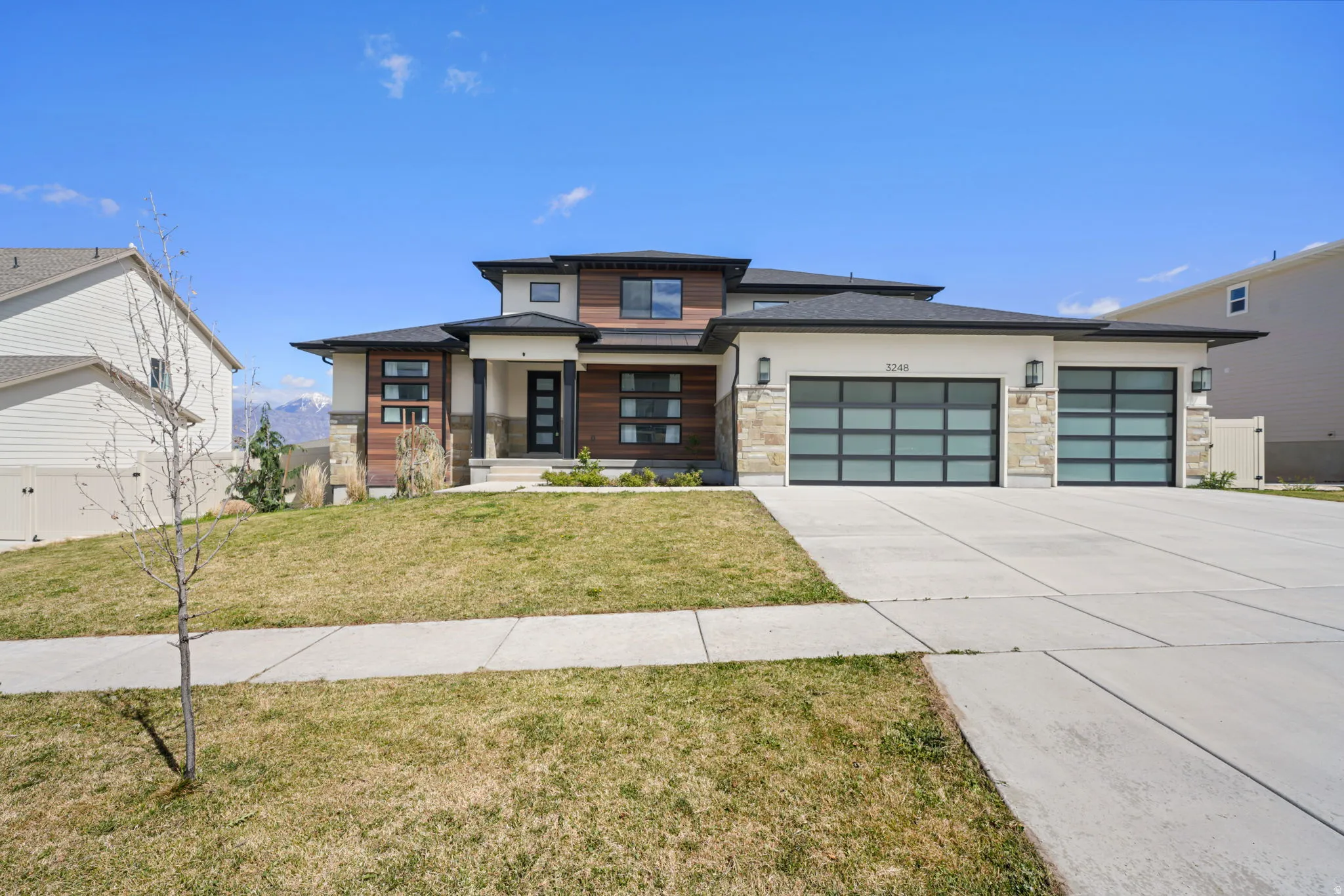 Prairie-style home featuring stone siding, a front lawn, a garage, concrete driveway, and covered porch