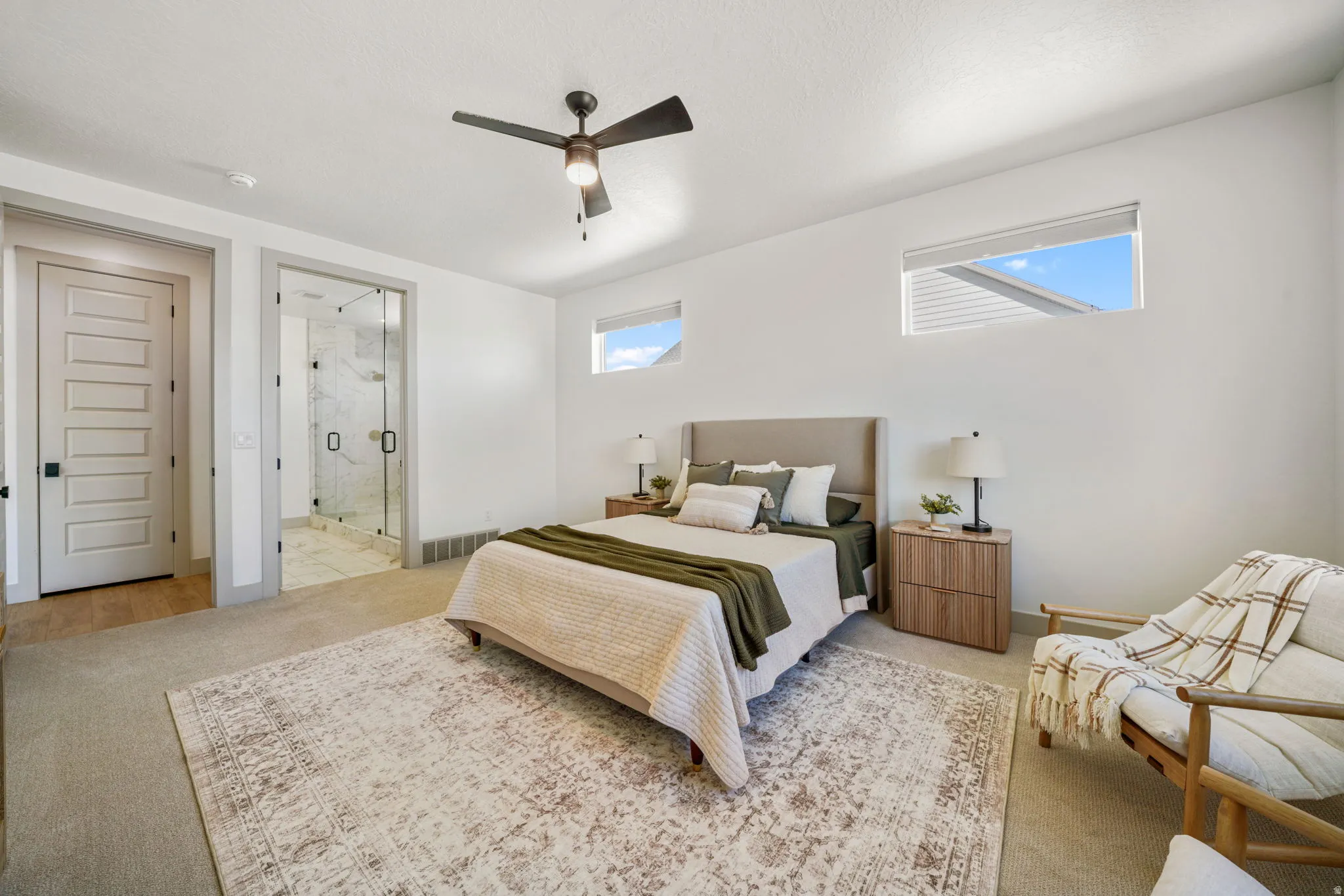 Bedroom with light carpet, connected bathroom, multiple windows, and ceiling fan