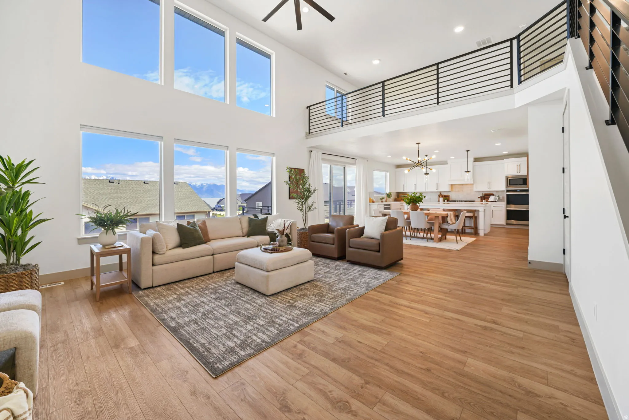 Living room with a high ceiling, hanging lights, ceiling fan, and light wood finished floors