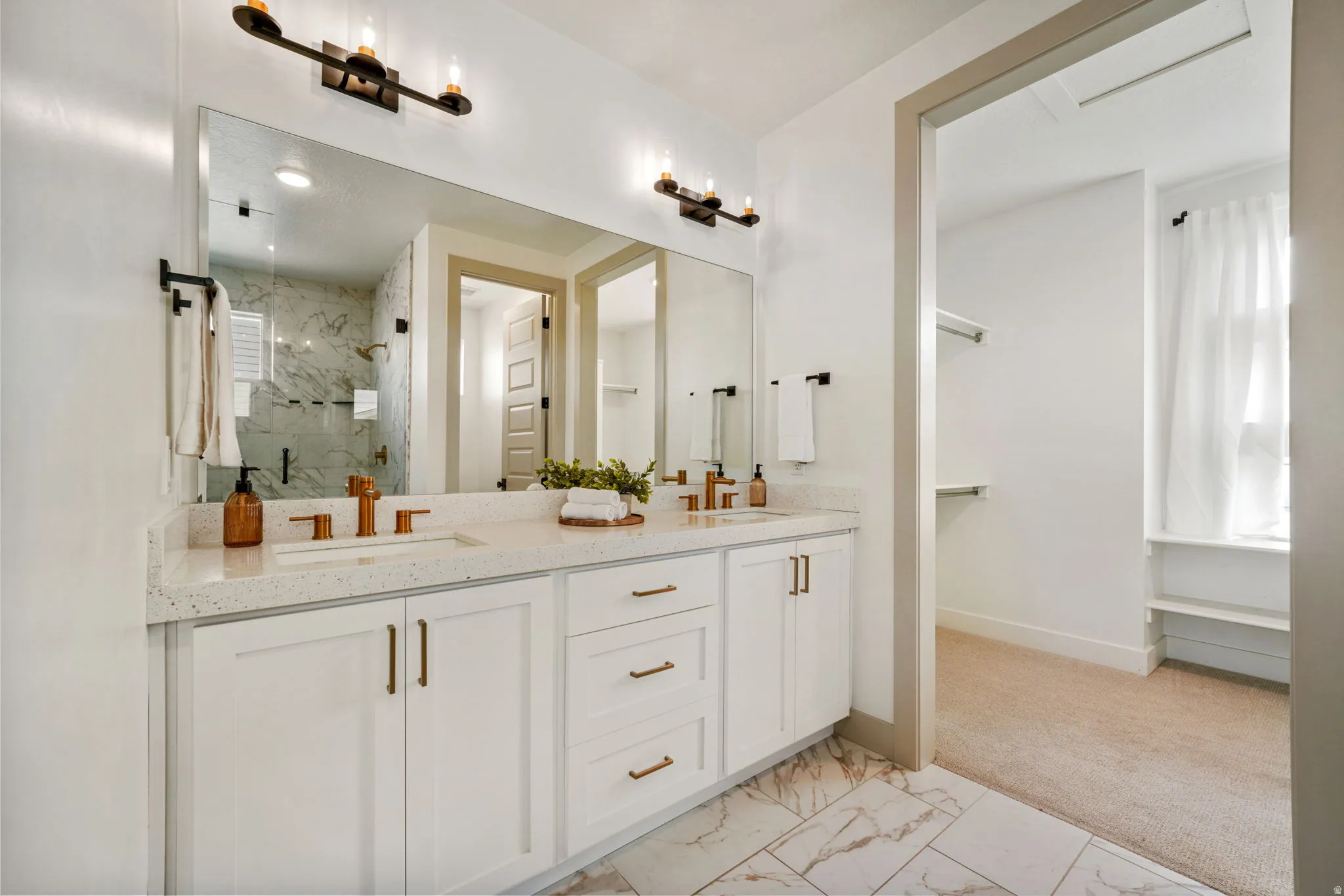 Full bath featuring light marble finish floors, double vanity, a marble finish shower, and light colored carpet