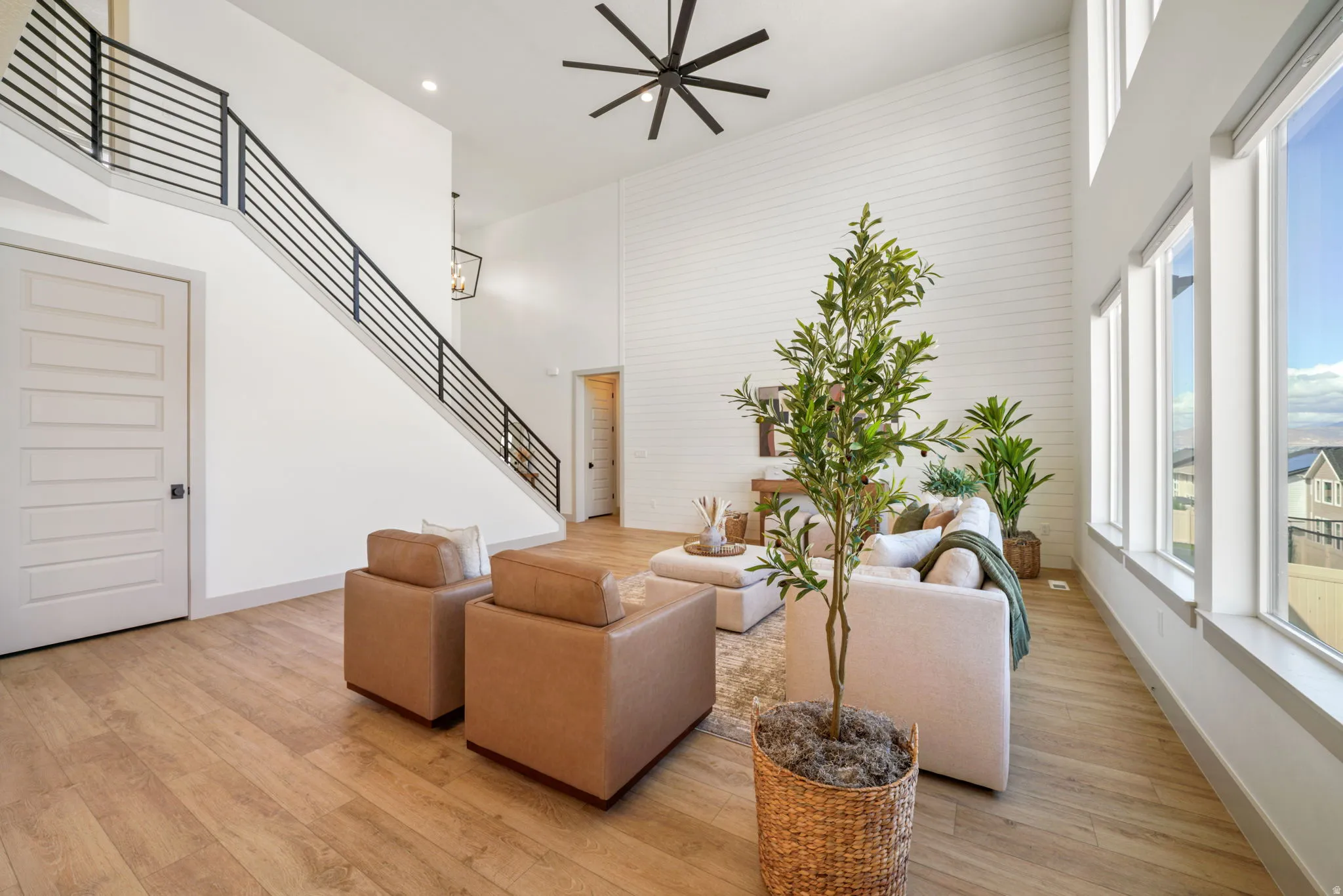 Living room with a high ceiling, a ceiling fan, and light wood-style floors