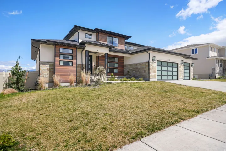 View of front of house with stone siding, a front yard, a garage, and driveway