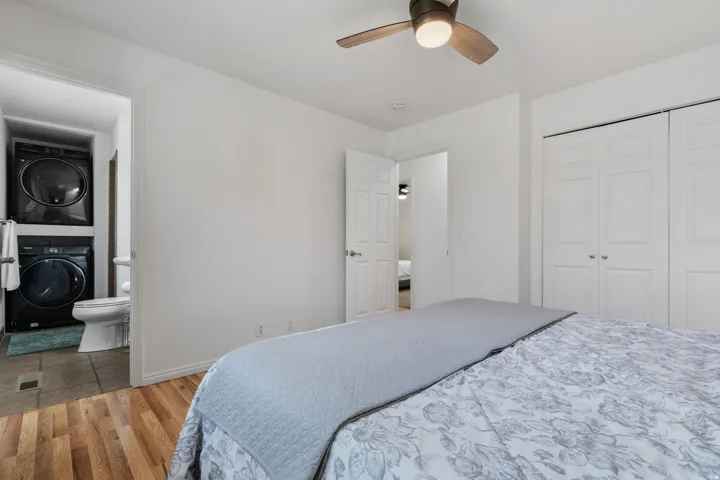 Bedroom featuring stacked washer / dryer, light wood-type flooring, ceiling fan, a closet, and ensuite bath