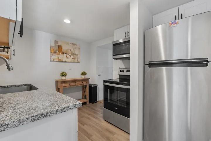 Kitchen featuring stainless steel appliances, white cabinetry, light stone counters, light wood-style flooring, and recessed lighting