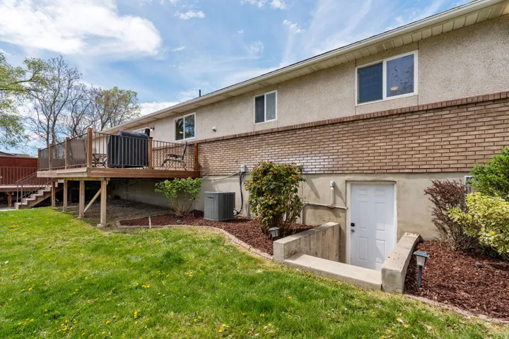 Back of house featuring stucco siding, brick siding, a wooden deck, and a yard