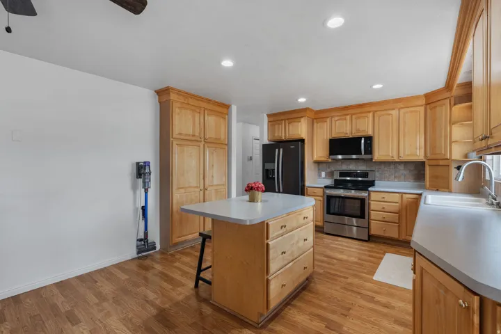 Kitchen with stainless steel appliances, a ceiling fan, decorative backsplash, light countertops, and a breakfast bar area