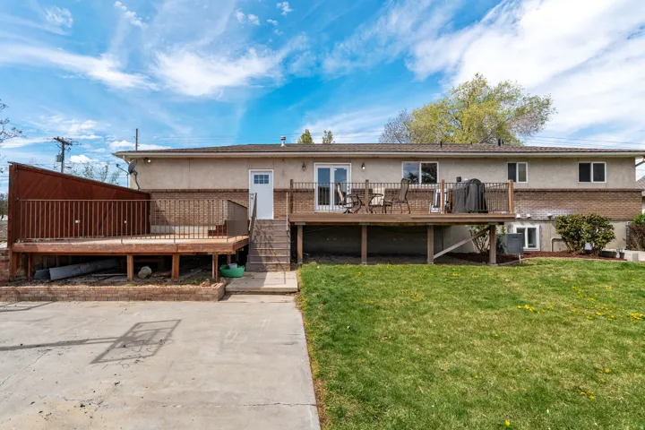 Back of property with stucco siding, a deck, a lawn, and brick siding