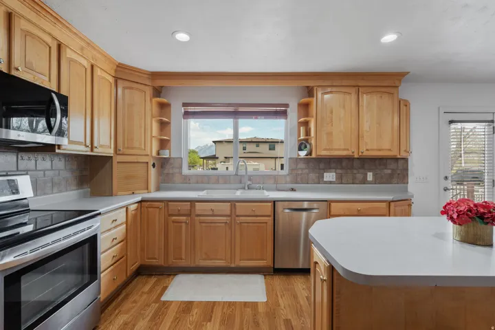 Kitchen with stainless steel appliances, open shelves, light countertops, light wood-style flooring, and decorative backsplash