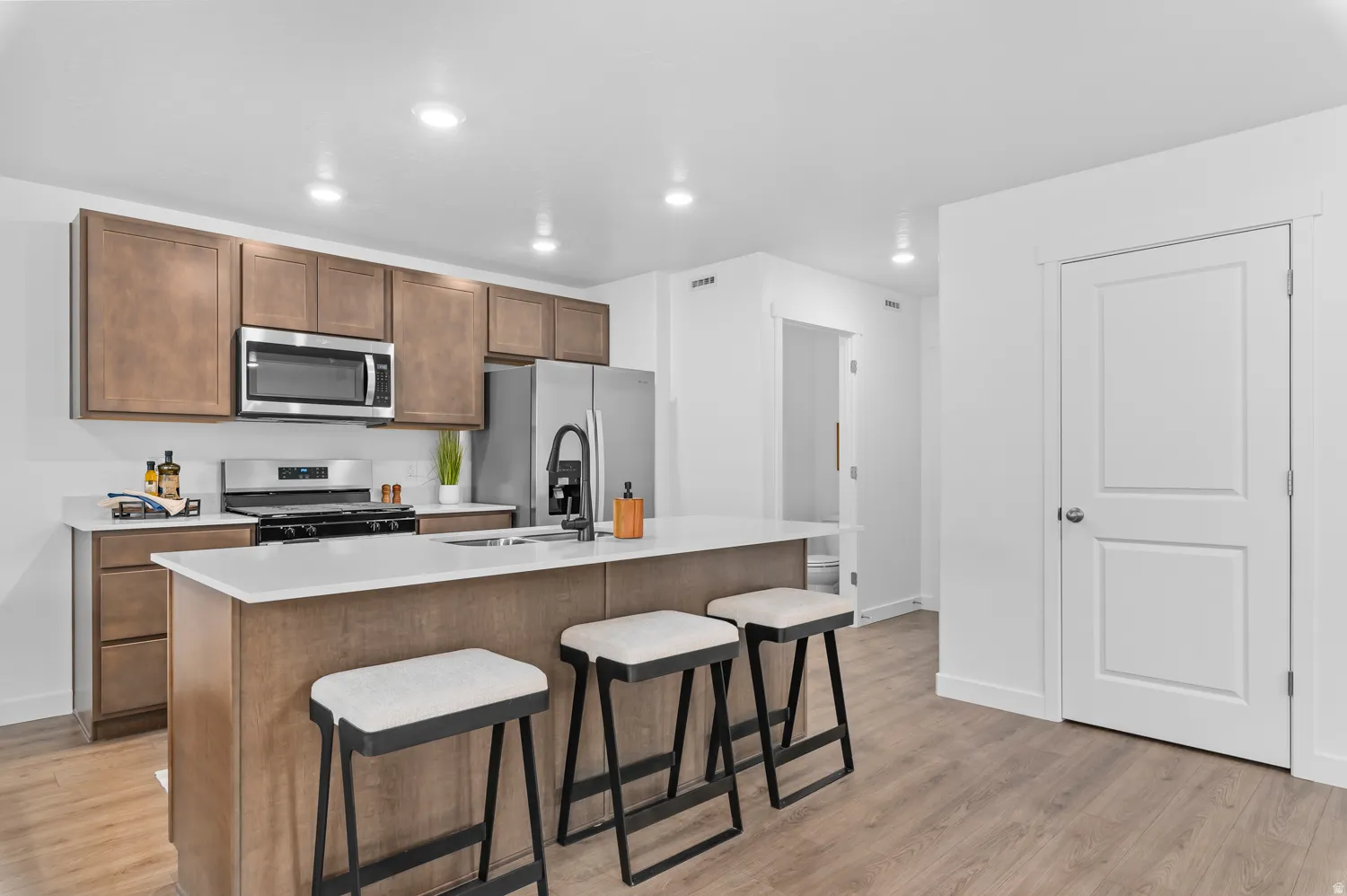 Kitchen with a kitchen breakfast bar, a kitchen island with sink, stainless steel appliances, light wood finished floors, and recessed lighting