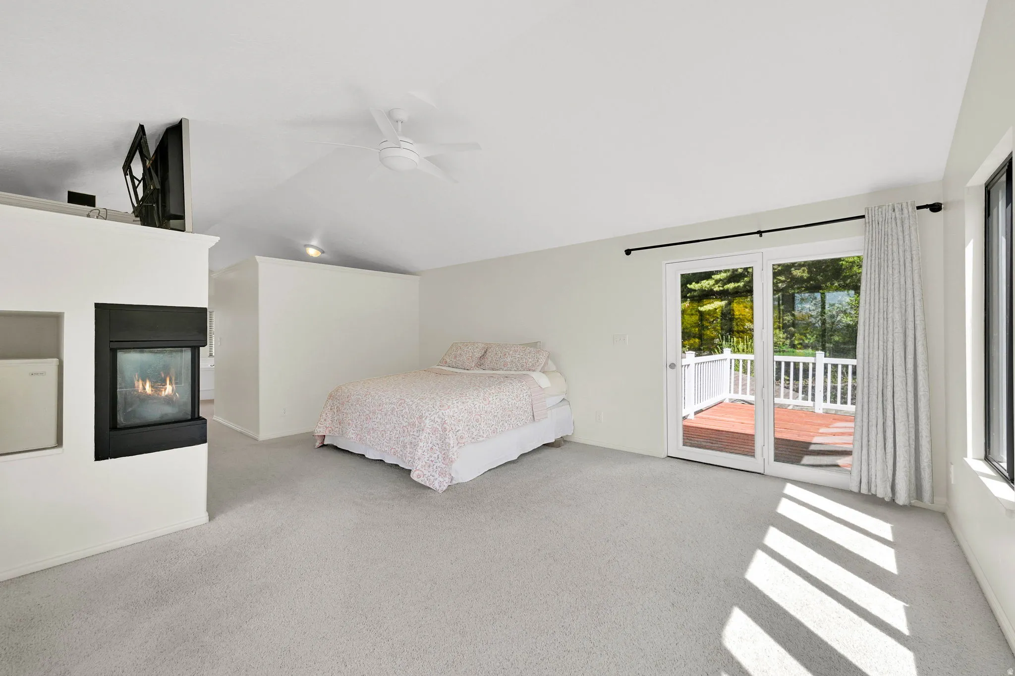 Bedroom with access to outside, light colored carpet, a multi sided fireplace, vaulted ceiling, and ceiling fan