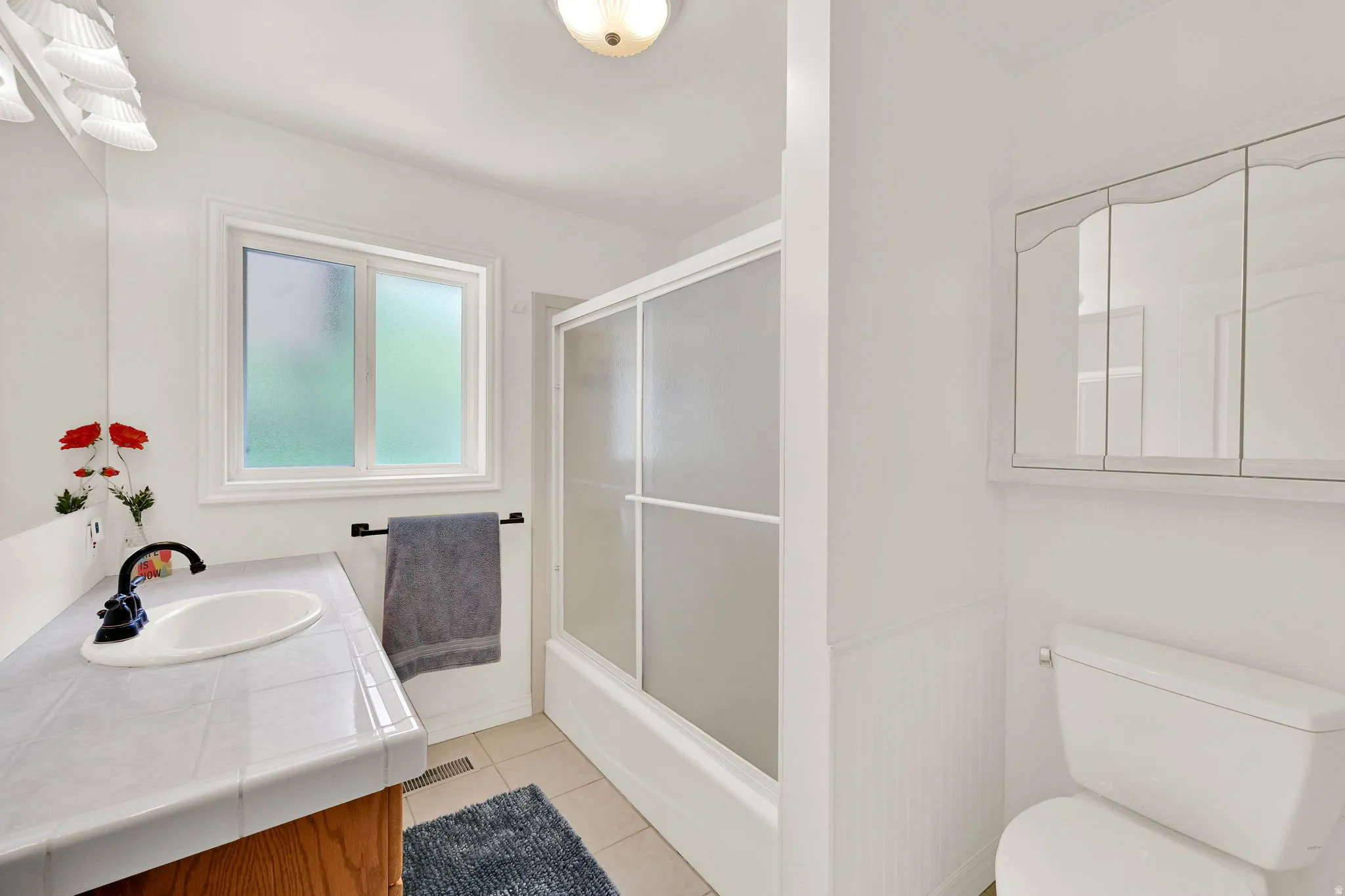 Bathroom featuring vanity, light tile patterned floors, and bath / shower combo with glass door