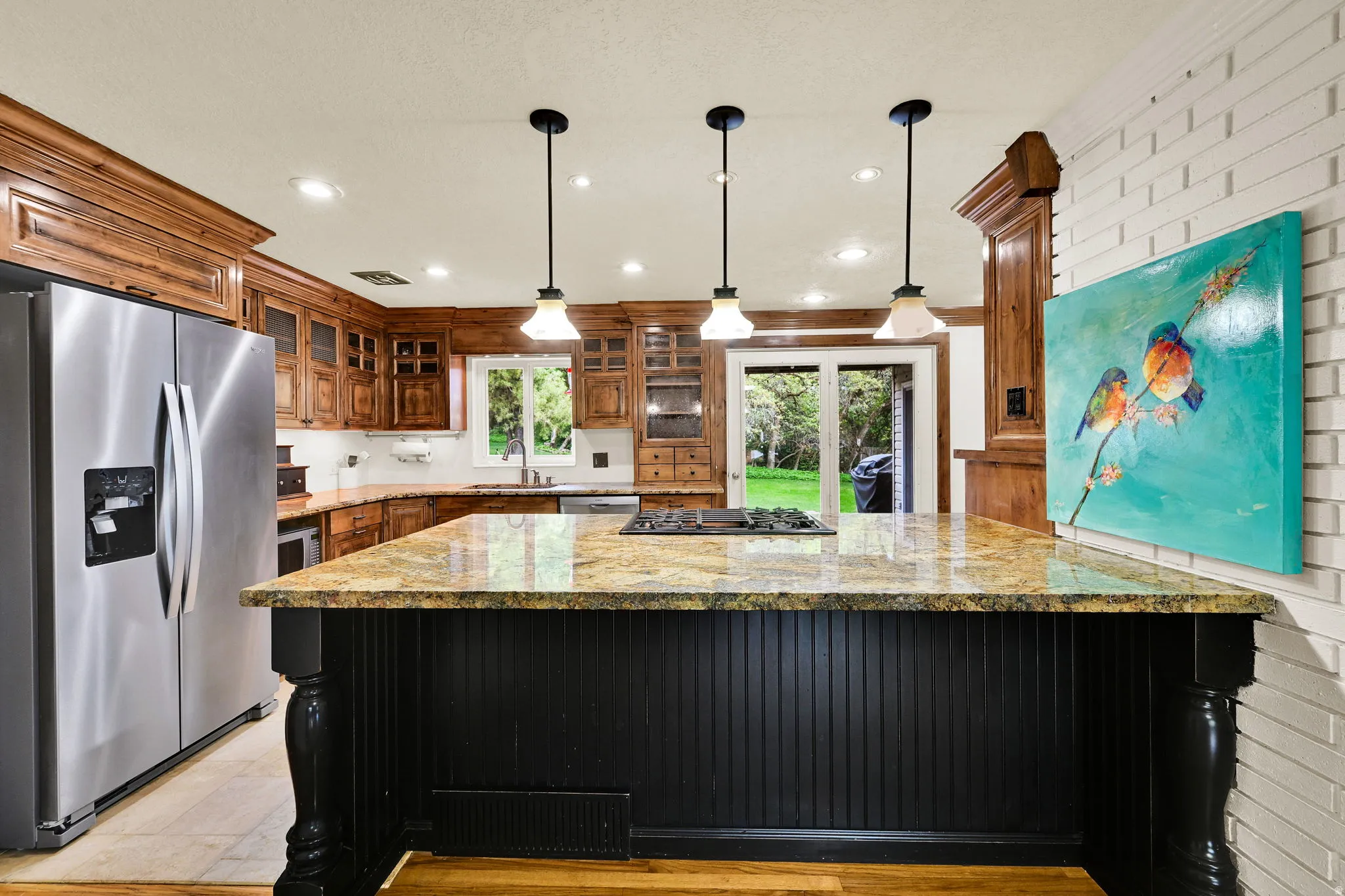 Kitchen featuring stainless steel appliances, light stone counters, pendant lighting, glass insert cabinets, and dark cabinetry