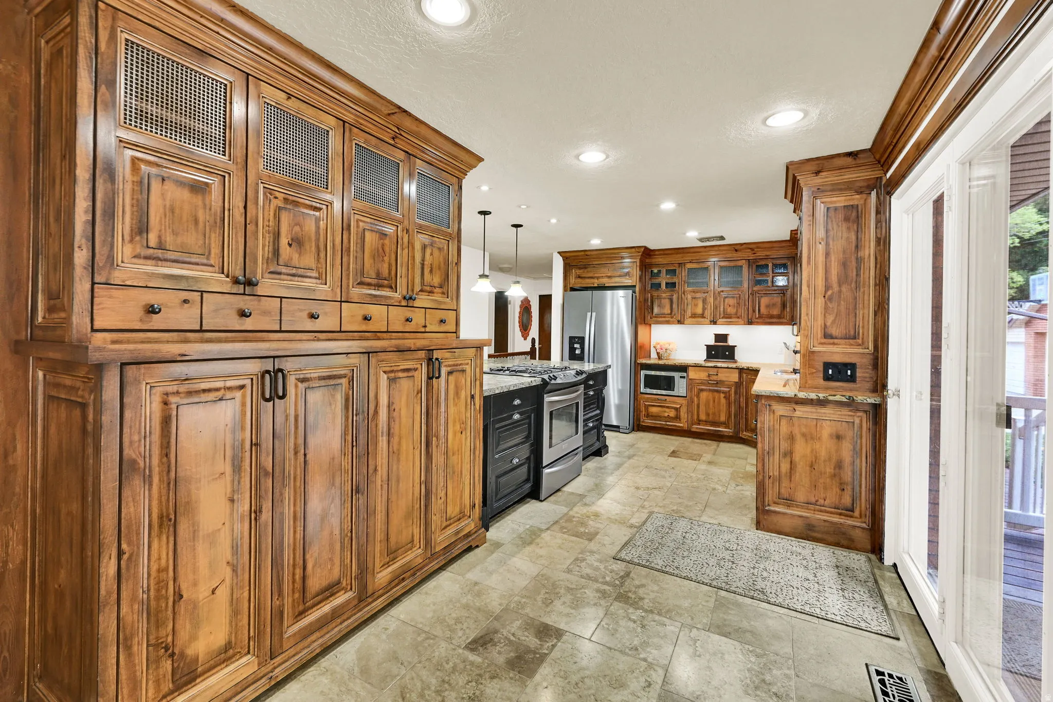 Kitchen featuring glass fronted cabinets, wood finish cabinets, decorative light fixtures, stainless steel appliances, and light stone counters