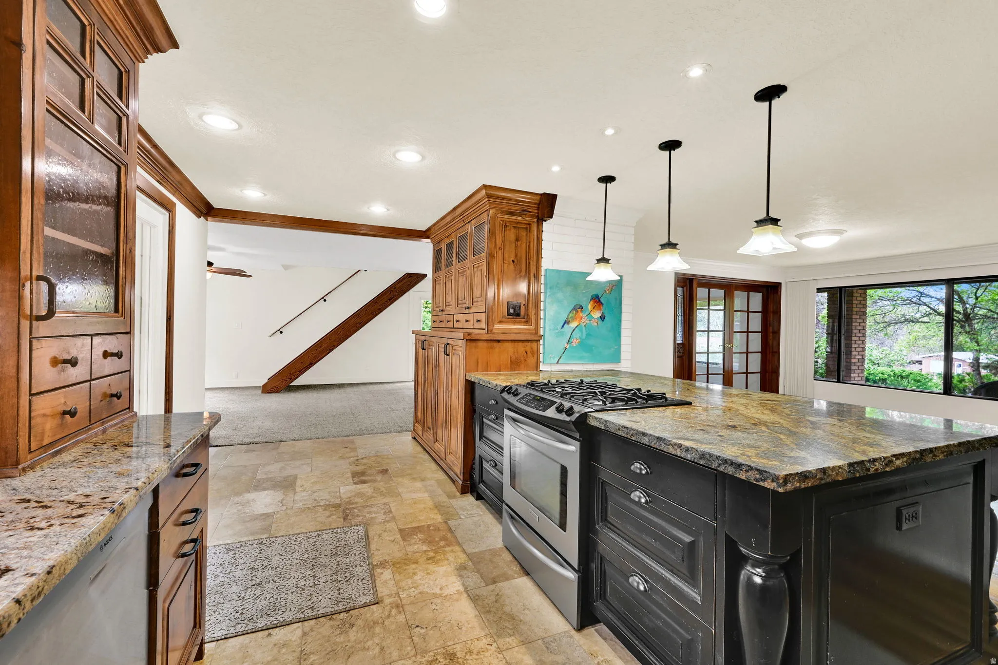 Two tone kitchen with glass fronted cabinets, stainless steel appliances, stone tile flooring, dark stone countertops, and ornamental molding