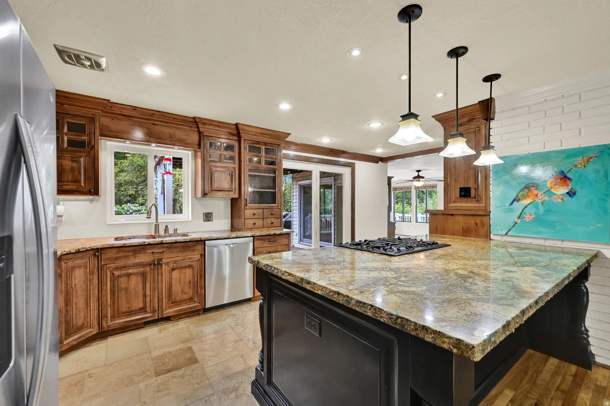 Dual tone kitchen with light stone countertops, stainless steel appliances, a kitchen island, glass insert cabinets, and hanging light fixtures