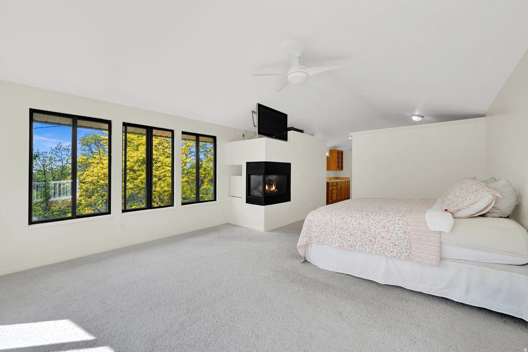 Carpeted bedroom featuring lofted ceiling, a multi sided fireplace, and ceiling fan