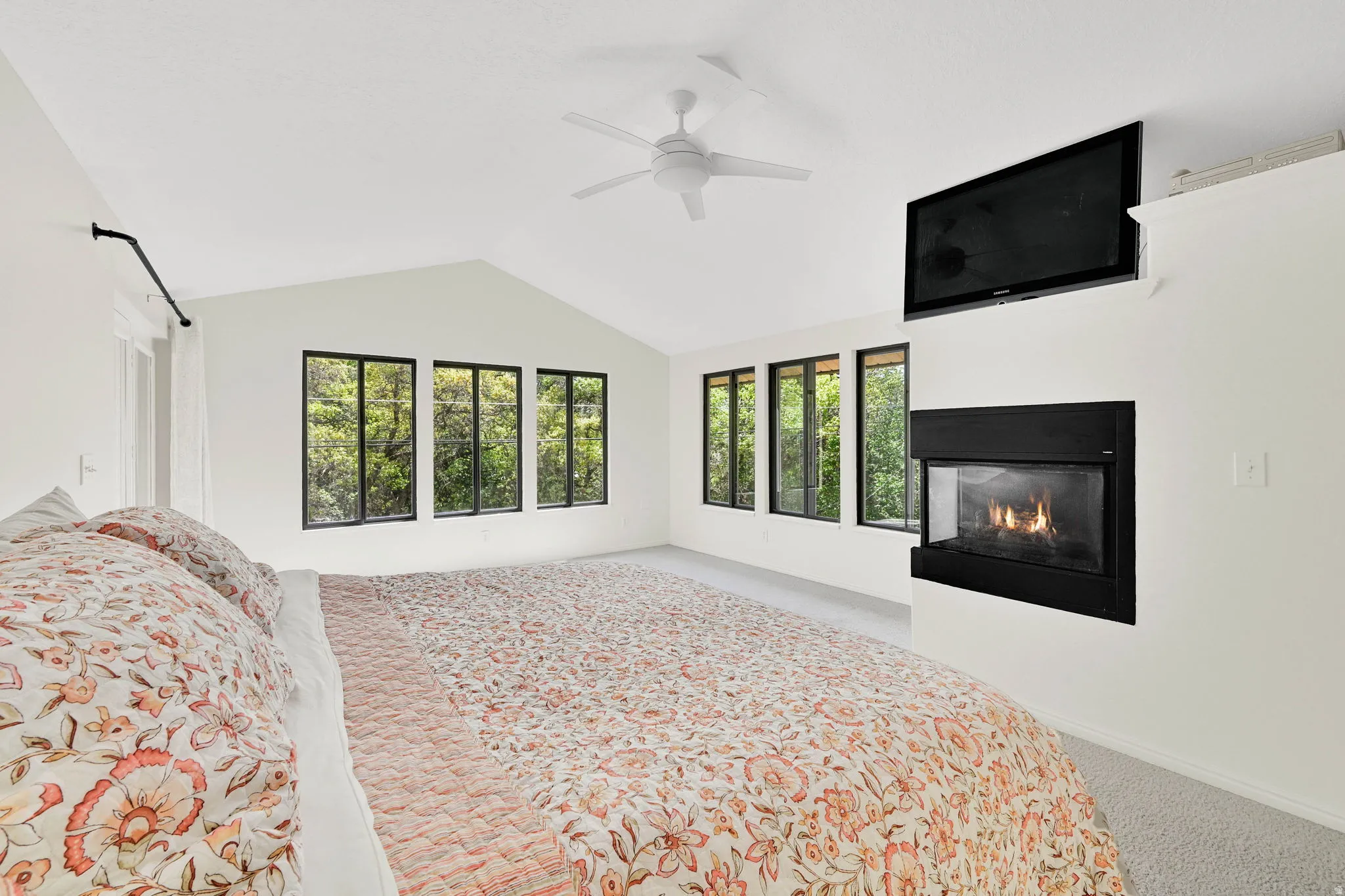 Bedroom with light carpet, a glass covered fireplace, and ceiling fan
